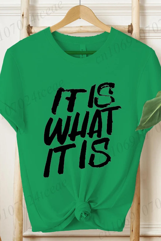 Green women's short sleeve T-shirt with IT IS WHAT IT IS sarcastic quote in bold black text, knotted at the hem, casual