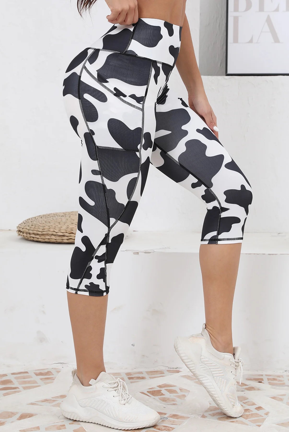 Women's Capri Yoga Pants with Pockets, high-waisted black and white cow print, stretchy athletic material, worn for workout.