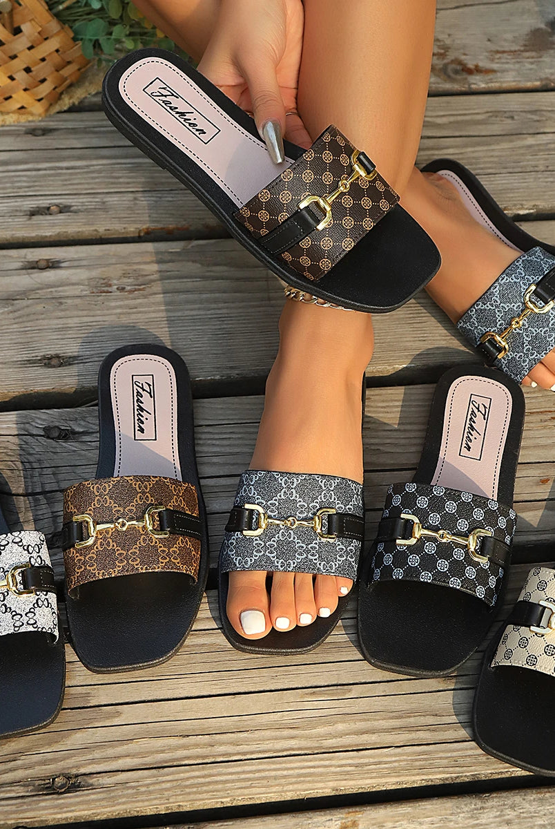 Spring and Summer women's slip-on sandals with patterned straps and gold buckle detail, in beige, brown, black, and white, on wooden deck.
