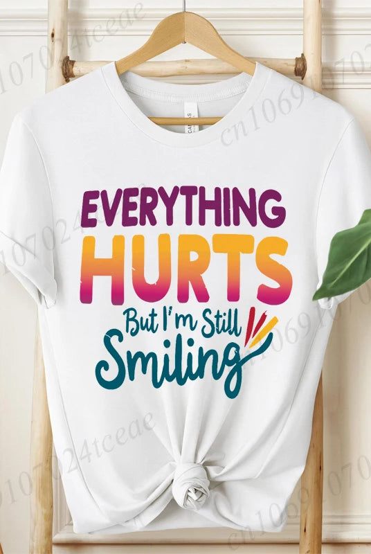 White cotton short sleeve T-shirt with Everything Hurts But I'm Still Smiling humorous sarcastic quote in purple, orange