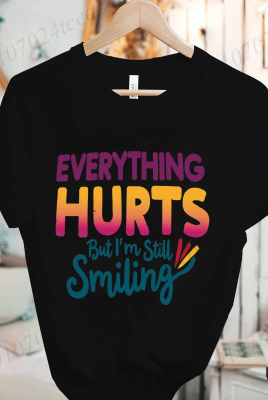 Black short sleeve T-shirt with colorful text reading Everything Hurts But I'm Still Smiling in casual font, suitable for