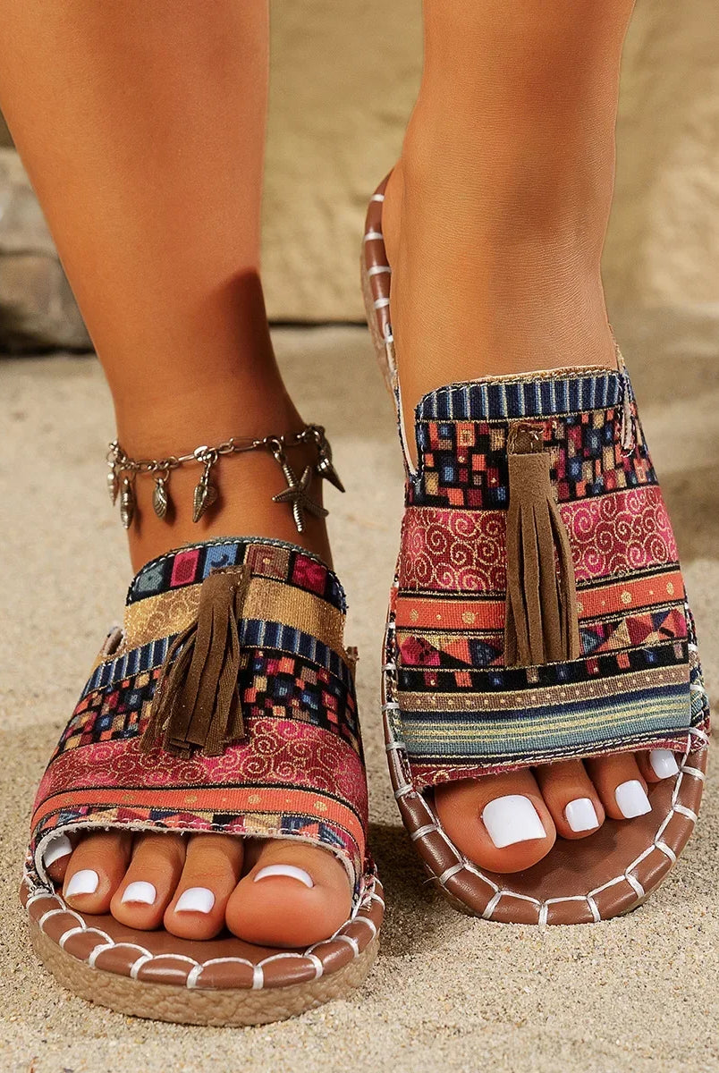 Bohemian flat bottom slippers women's outdoor summer sandals with colorful patchwork fabric, tassel detail, and flat sole on sandy beach.