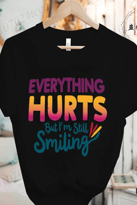 Black short-sleeve T-shirt with colorful text reading Everything Hurts But I'm Still Smiling from the Everything Hurts But