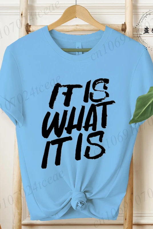 Light blue women's T-shirt with IT IS WHAT IT IS in bold black graphic text, short sleeves, casual summer fashion tee