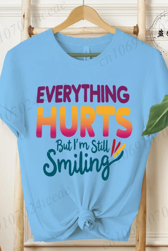Light blue short sleeve T-shirt with a knot at the hem featuring the Everything Hurts But I'm Still Smiling funny sarcastic
