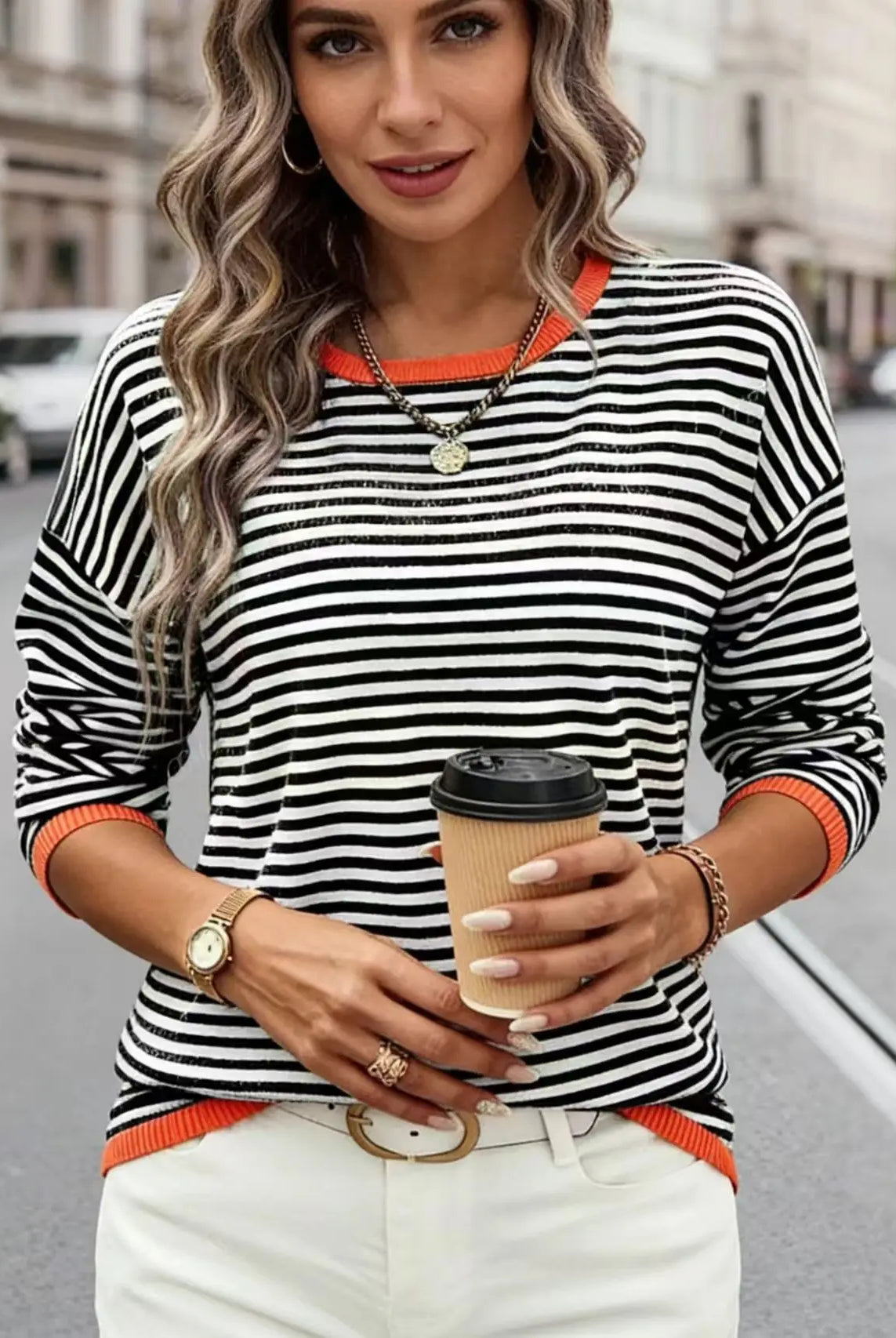 Plus-Size Women's Striped Color-Blocked Fashion Loose Sweater in black, white, and orange, worn with white pants, holding a