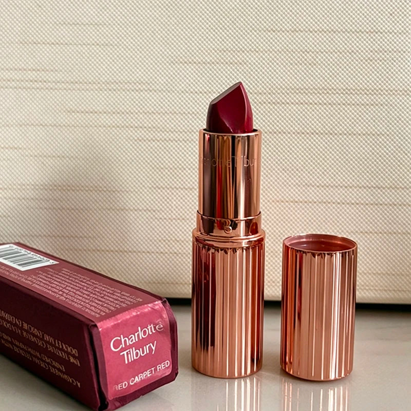 Charlotte Tilbury Walk of No Shame lipstick in a deep red shade with a rose gold tube, next to matching rose gold lip gloss