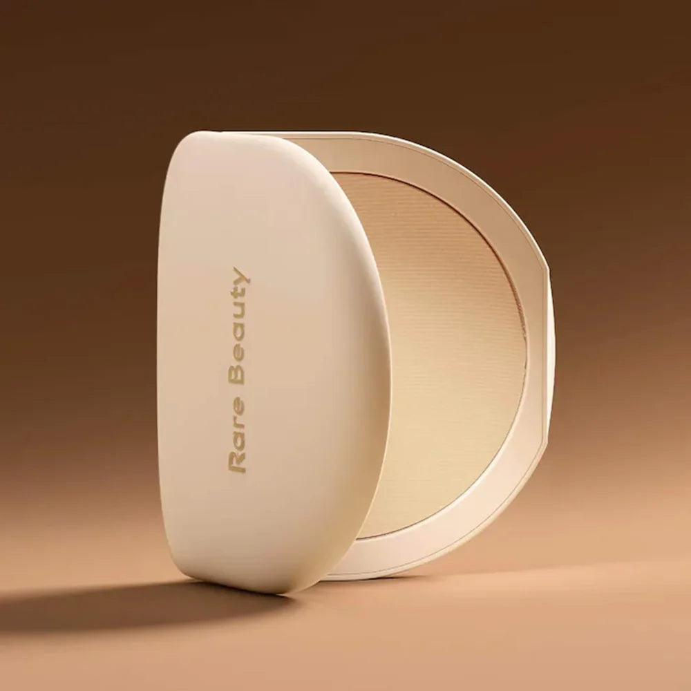 Rare Beauty Stay Genuine Shaded Compact Setting Powder in a beige round case with gold lettering, partially open to show the