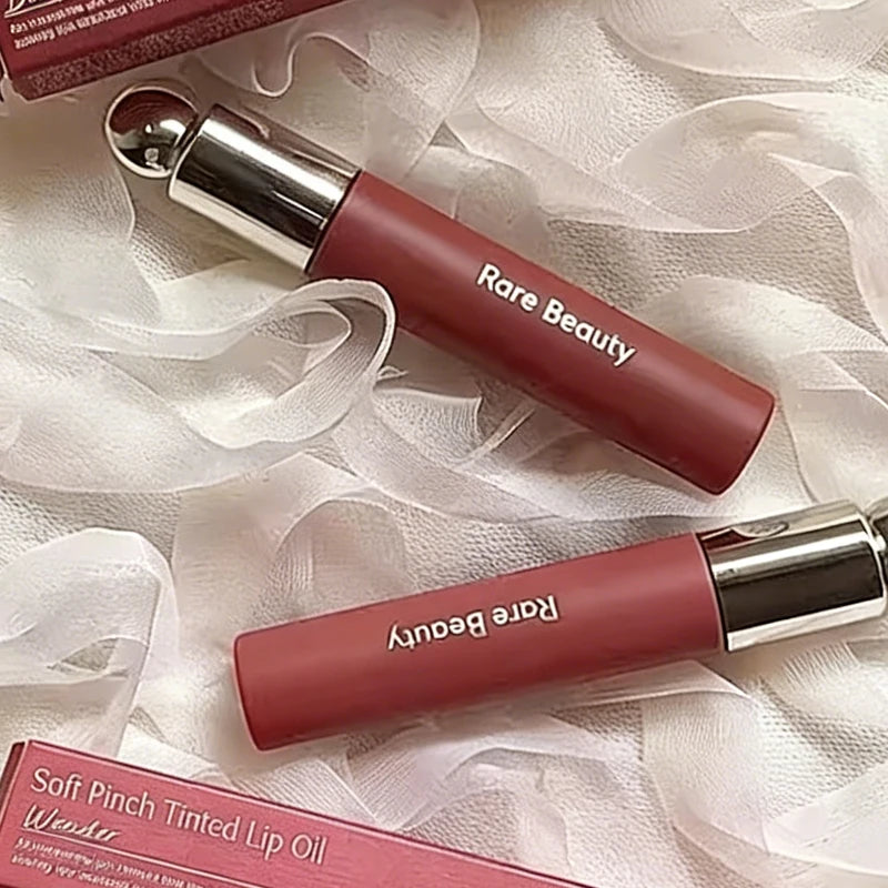 Rare Beauty 7-Colors Soft Pinch Tinted Lip Oil Stain Lip Gloss in natural pink shades with silver caps, lying on white